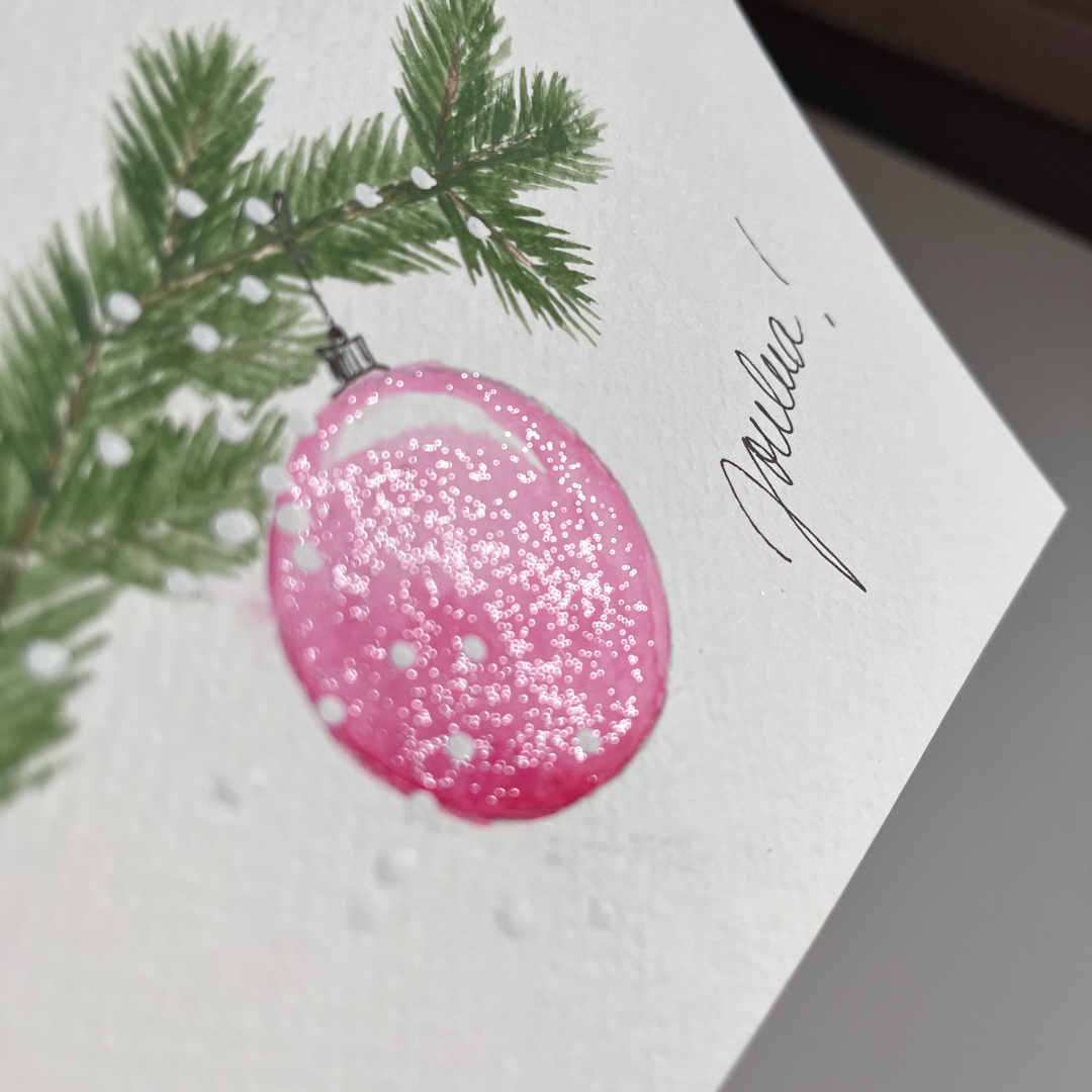 Lähikuva joulukortin joulupallosta, jossa hopeisen väristä kimalletta.