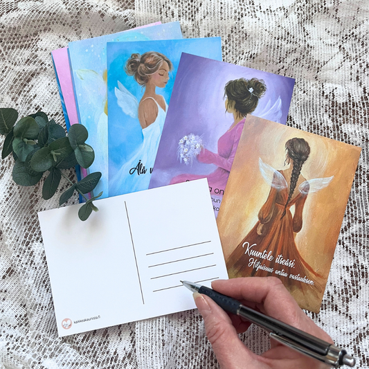 Enkelipostikortteja ja käsi, joka kirjoittaa kynällä korttiin.